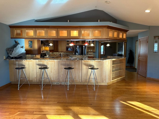 bar with lofted ceiling, black appliances, sink, dark stone countertops, and light wood-type flooring