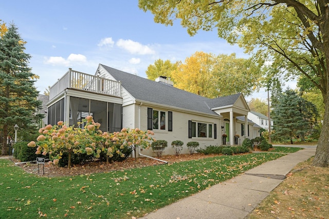 view of side of home featuring a balcony, a lawn, and a sunroom