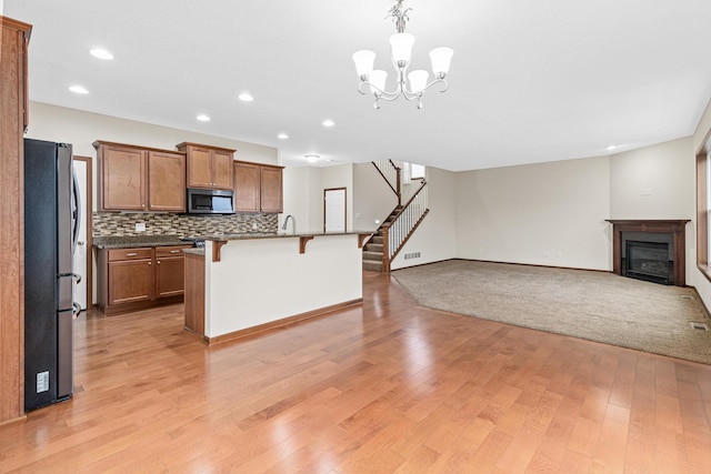 kitchen with a kitchen bar, appliances with stainless steel finishes, light hardwood / wood-style flooring, and a kitchen island with sink