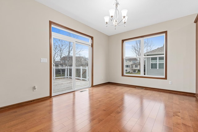 spare room with plenty of natural light, light wood-type flooring, and an inviting chandelier