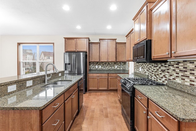 kitchen with light hardwood / wood-style flooring, black appliances, stone countertops, and sink