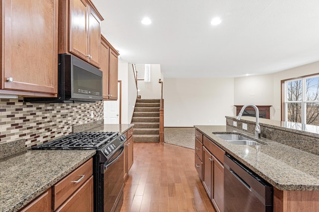 kitchen featuring a center island with sink, sink, light hardwood / wood-style flooring, light stone counters, and stainless steel appliances