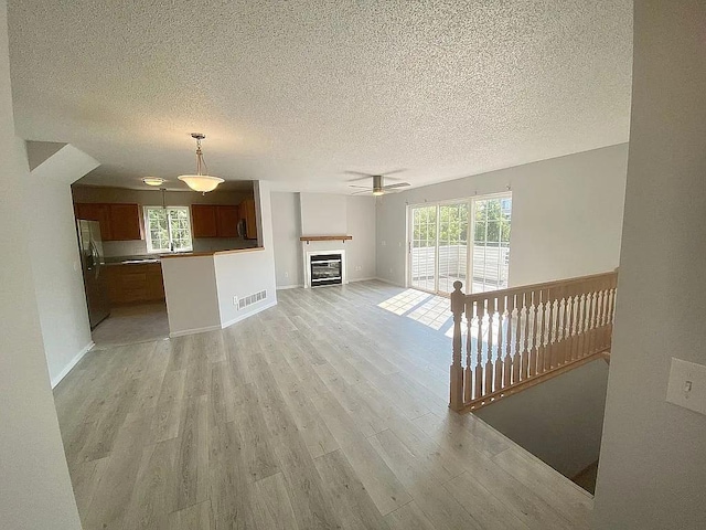 unfurnished living room featuring light wood-type flooring, a textured ceiling, and ceiling fan