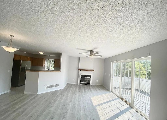 unfurnished living room featuring ceiling fan, a textured ceiling, and light hardwood / wood-style floors