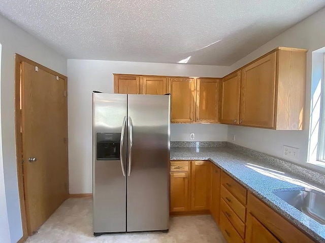 kitchen featuring stainless steel fridge, a textured ceiling, sink, and light stone counters