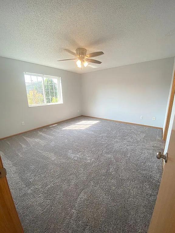 empty room featuring ceiling fan, a textured ceiling, and carpet floors