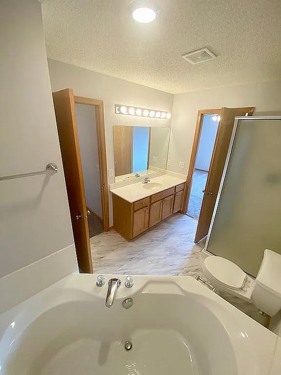 full bathroom with vanity, a textured ceiling, shower with separate bathtub, and toilet