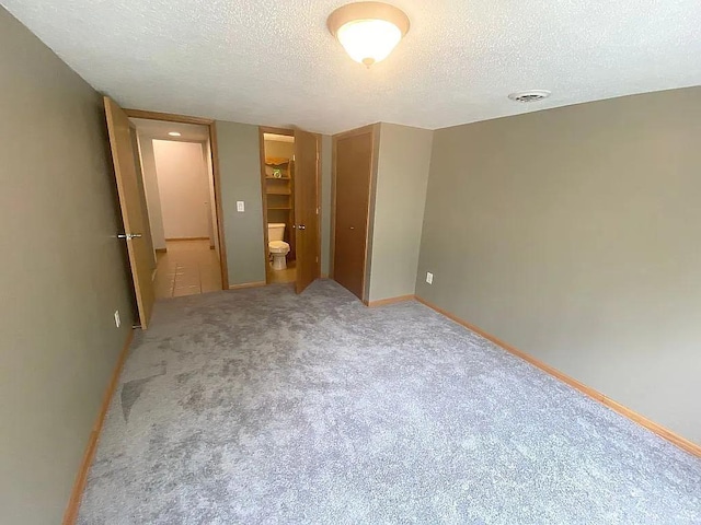 unfurnished bedroom with ensuite bathroom, a textured ceiling, a closet, and carpet