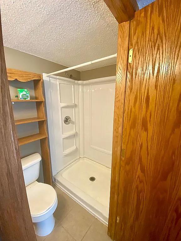 bathroom with tile patterned flooring, a textured ceiling, toilet, and a shower