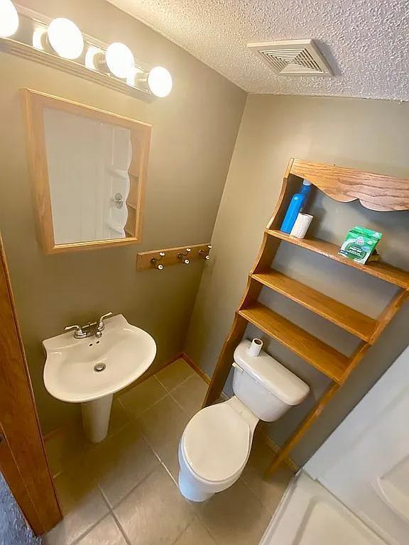 bathroom featuring toilet, a textured ceiling, tile patterned floors, and sink