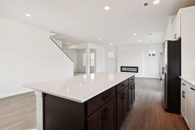 kitchen with stainless steel fridge, white cabinetry, a kitchen island, and hardwood / wood-style floors