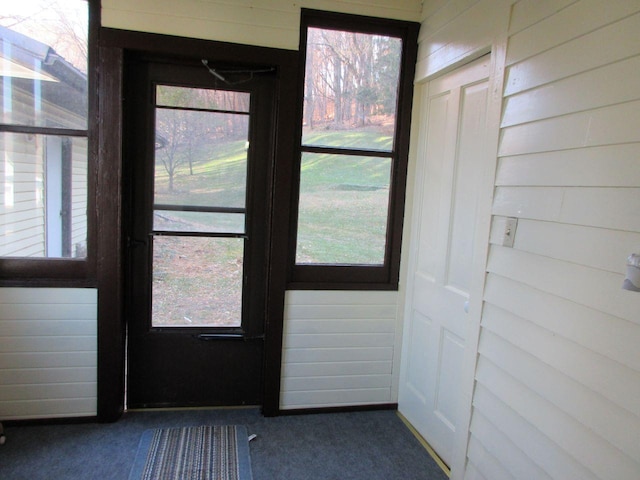 doorway to outside featuring wooden walls, plenty of natural light, and dark colored carpet