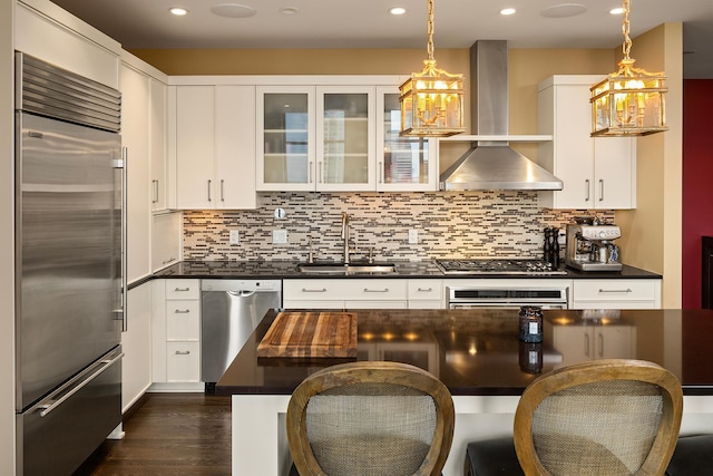 kitchen with stainless steel appliances, sink, wall chimney exhaust hood, decorative light fixtures, and white cabinets