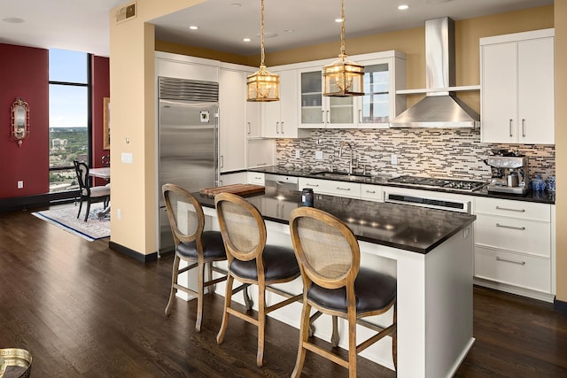 kitchen featuring stainless steel appliances, a kitchen island, white cabinetry, dark wood-type flooring, and wall chimney exhaust hood