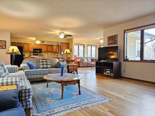 living room with ceiling fan, light hardwood / wood-style flooring, and a textured ceiling