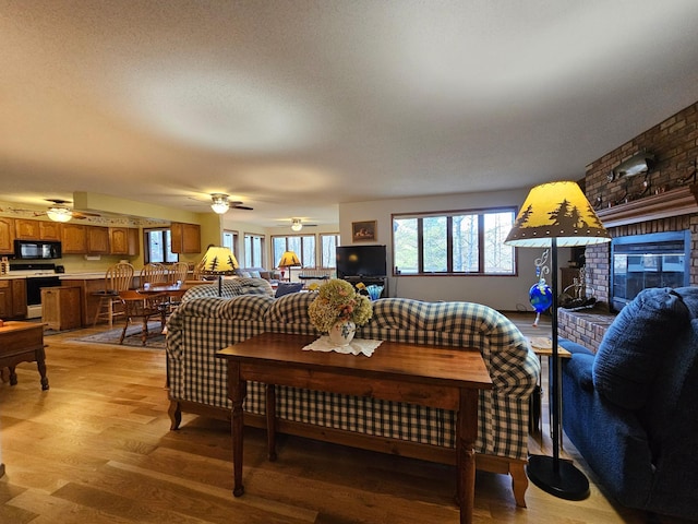 living room featuring a brick fireplace, ceiling fan, a textured ceiling, and light wood-type flooring