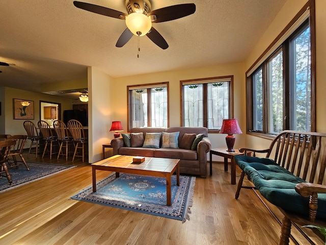 living area with a textured ceiling, ceiling fan, healthy amount of natural light, and wood finished floors