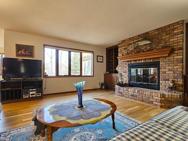 living area featuring a textured ceiling, wood finished floors, built in features, a brick fireplace, and baseboards