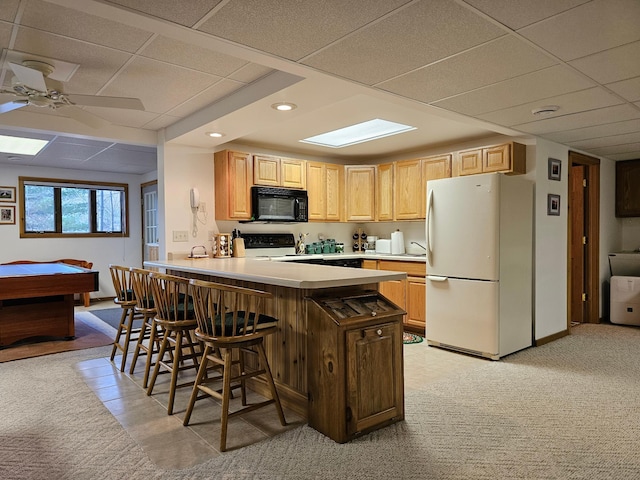 kitchen featuring freestanding refrigerator, black microwave, a drop ceiling, stove, and a kitchen breakfast bar