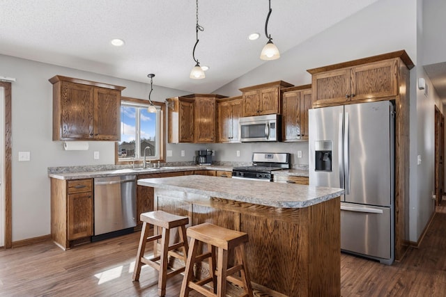 kitchen featuring lofted ceiling, appliances with stainless steel finishes, a center island, hanging light fixtures, and a sink