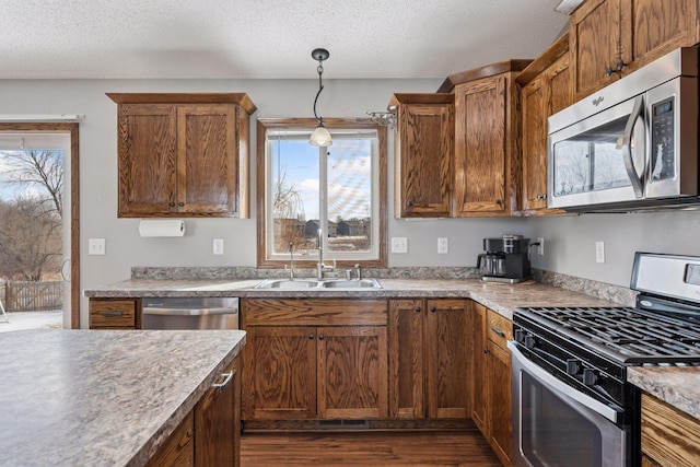 kitchen featuring a textured ceiling, hanging light fixtures, appliances with stainless steel finishes, and a sink