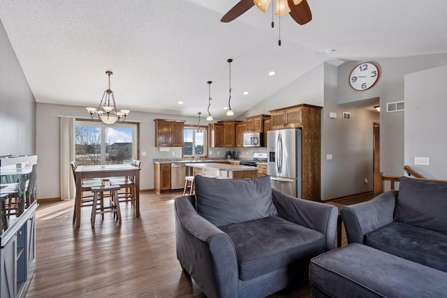 living room featuring ceiling fan with notable chandelier, wood finished floors, visible vents, baseboards, and vaulted ceiling