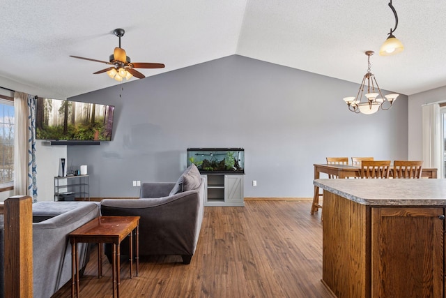 living room with dark wood-type flooring, vaulted ceiling, a textured ceiling, baseboards, and ceiling fan with notable chandelier