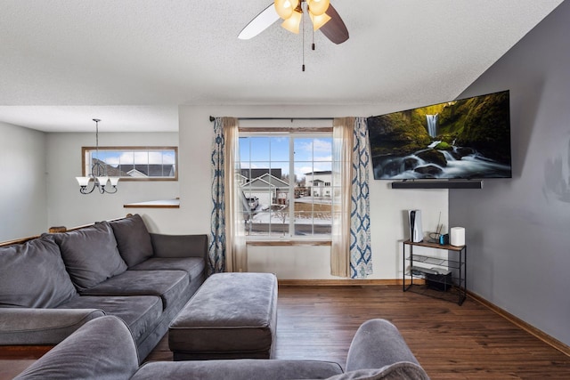 living area featuring ceiling fan with notable chandelier, a textured ceiling, baseboards, and wood finished floors