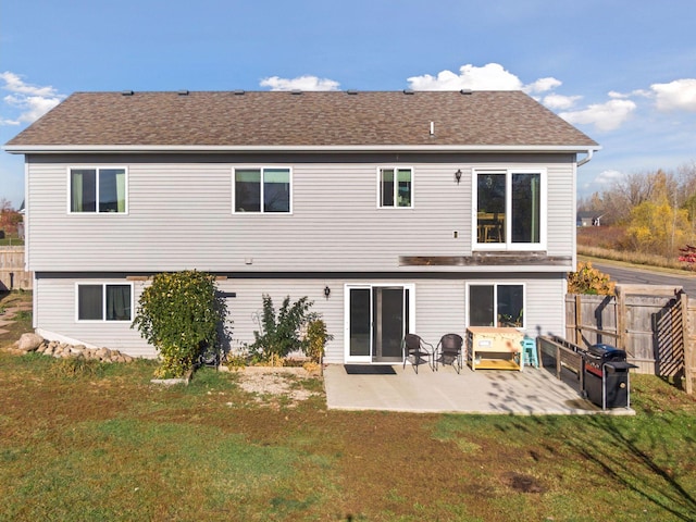 back of property with a shingled roof, a patio area, a lawn, and fence