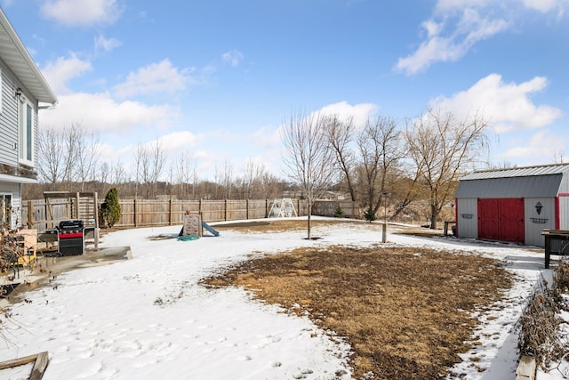 yard layered in snow with a garage, a storage shed, fence, and an outdoor structure