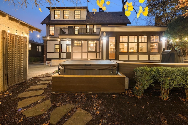 back house at dusk with a balcony and a hot tub