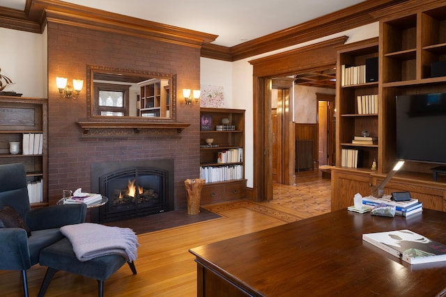 living room featuring built in shelves, light wood-type flooring, crown molding, and a brick fireplace