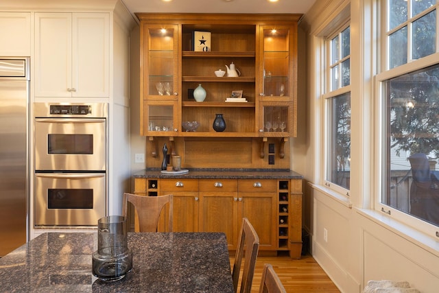 bar featuring light wood-type flooring, stainless steel appliances, and dark stone counters