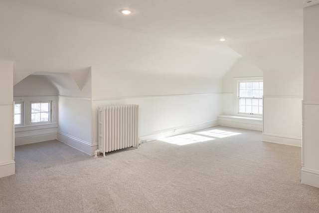 additional living space with plenty of natural light, light carpet, radiator heating unit, and vaulted ceiling