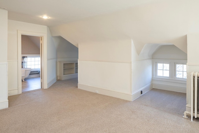 bonus room with radiator, light colored carpet, and vaulted ceiling