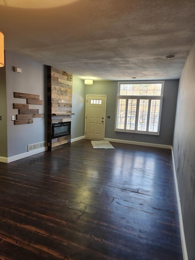 unfurnished living room with a fireplace, a textured ceiling, and dark wood-type flooring