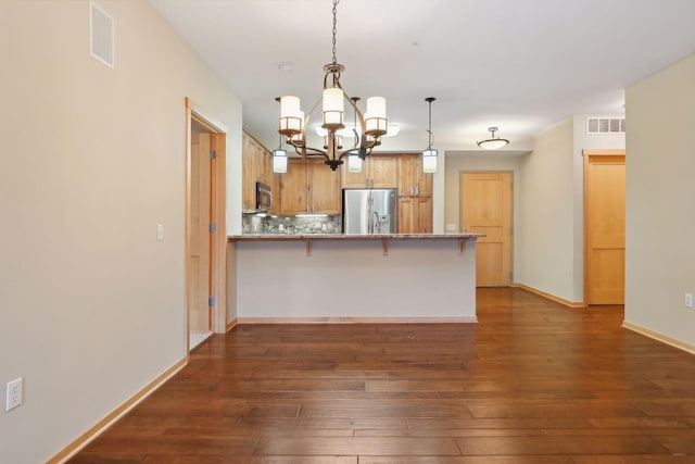 kitchen featuring kitchen peninsula, appliances with stainless steel finishes, a breakfast bar area, decorative light fixtures, and dark hardwood / wood-style flooring