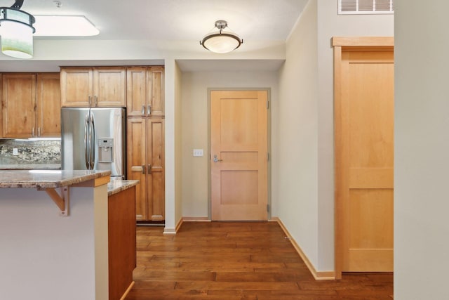 kitchen with light stone countertops, stainless steel refrigerator with ice dispenser, decorative backsplash, a breakfast bar area, and dark wood-type flooring