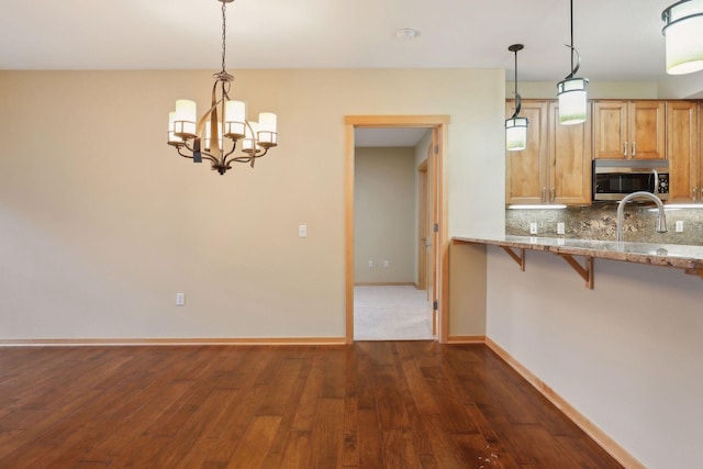 kitchen with dark wood-type flooring, tasteful backsplash, hanging light fixtures, and a breakfast bar area