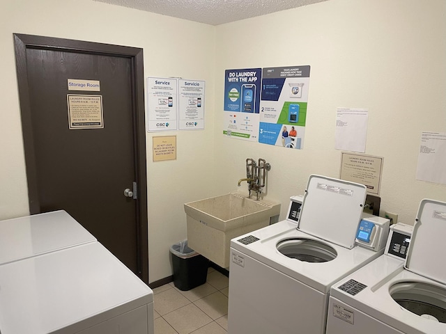 laundry room featuring washing machine and dryer, a textured ceiling, sink, and light tile patterned flooring