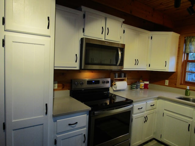 kitchen with wood walls, white cabinetry, sink, and appliances with stainless steel finishes