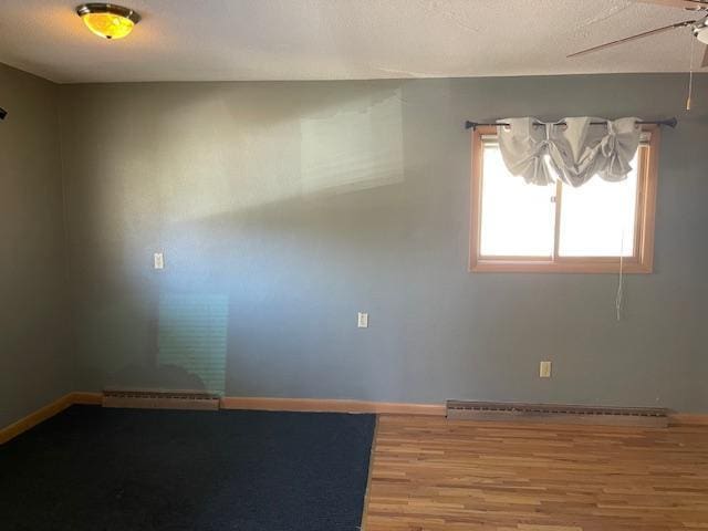 unfurnished room with hardwood / wood-style floors, a baseboard heating unit, and ceiling fan