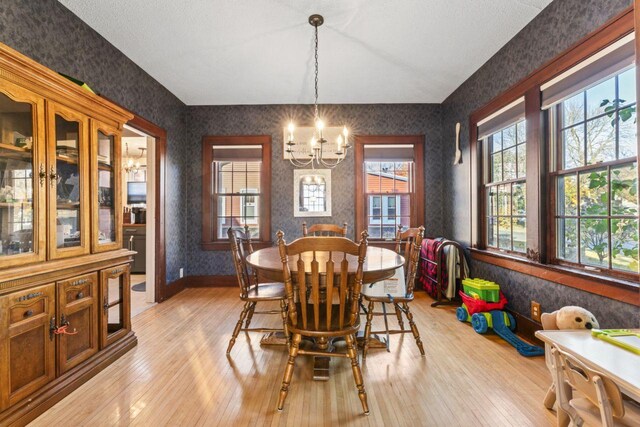 dining area with light hardwood / wood-style flooring, a textured ceiling, and an inviting chandelier