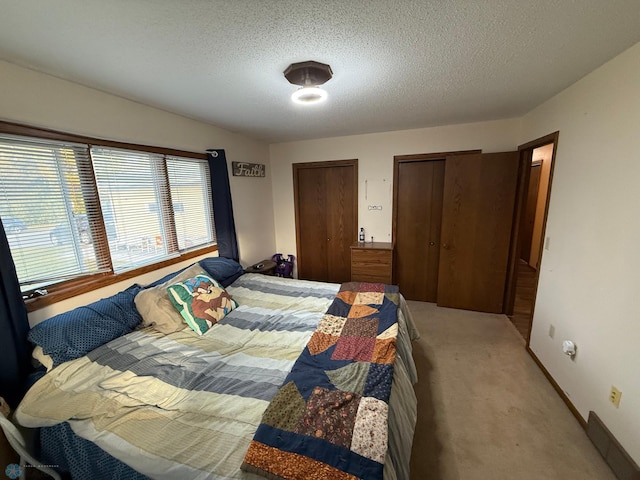 bedroom featuring two closets, light carpet, and a textured ceiling