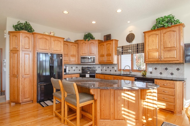 kitchen featuring light hardwood / wood-style flooring, stainless steel appliances, dark stone counters, sink, and a center island