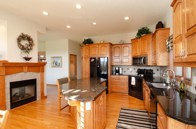 kitchen featuring black appliances, sink, light wood-type flooring, a kitchen island, and a tile fireplace