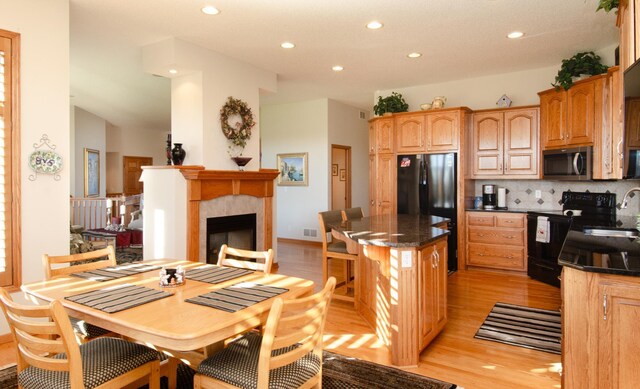 kitchen featuring decorative backsplash, light hardwood / wood-style flooring, a tile fireplace, sink, and black appliances