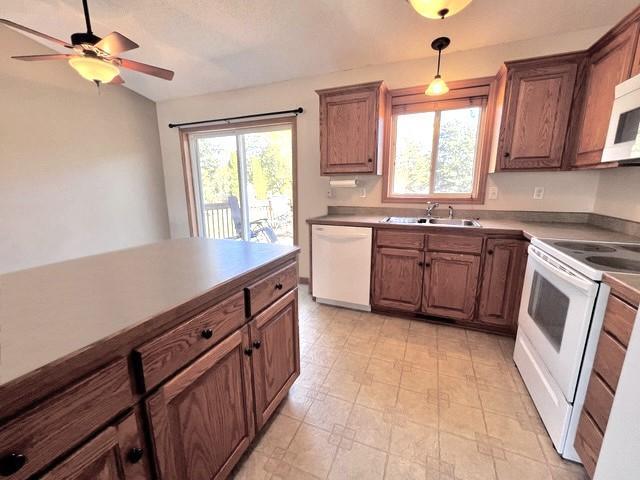 kitchen featuring white appliances, plenty of natural light, pendant lighting, and a sink