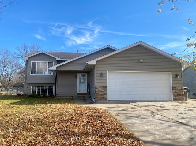 split level home with an attached garage, stone siding, and driveway