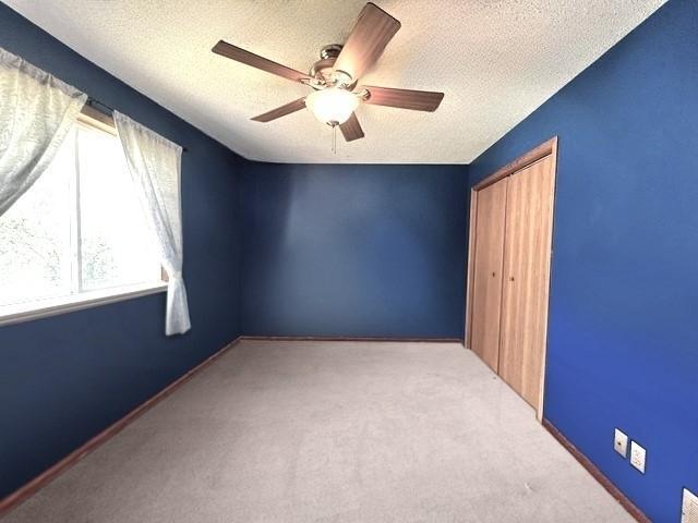 carpeted spare room with a textured ceiling, ceiling fan, and baseboards